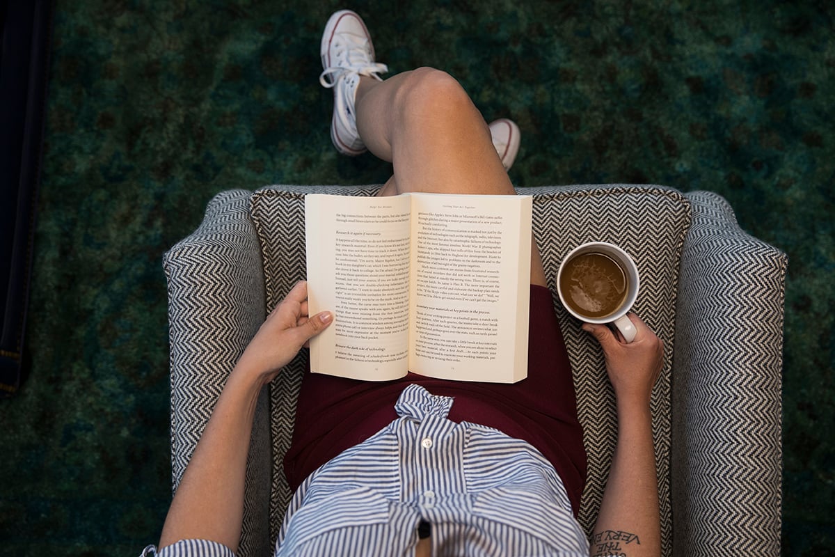 A woman reads a book while sipping on coffee.