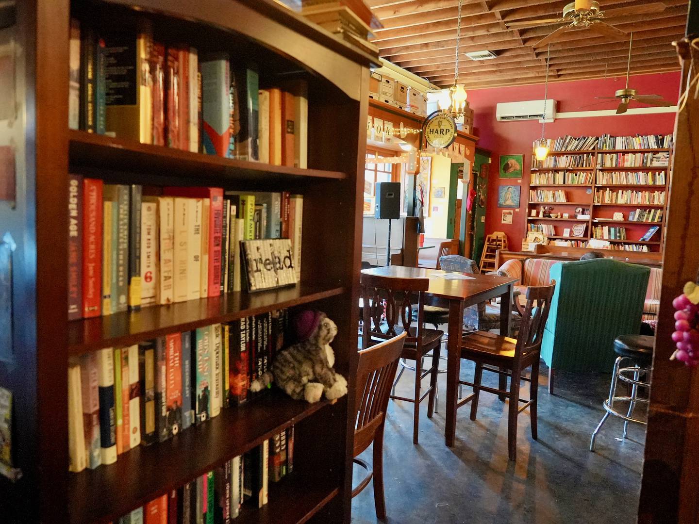 a bookshelf in the foreground with tables and armchairs of a cozy pub in the background