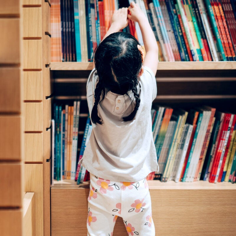 Small child choosing books from a bookshelf.