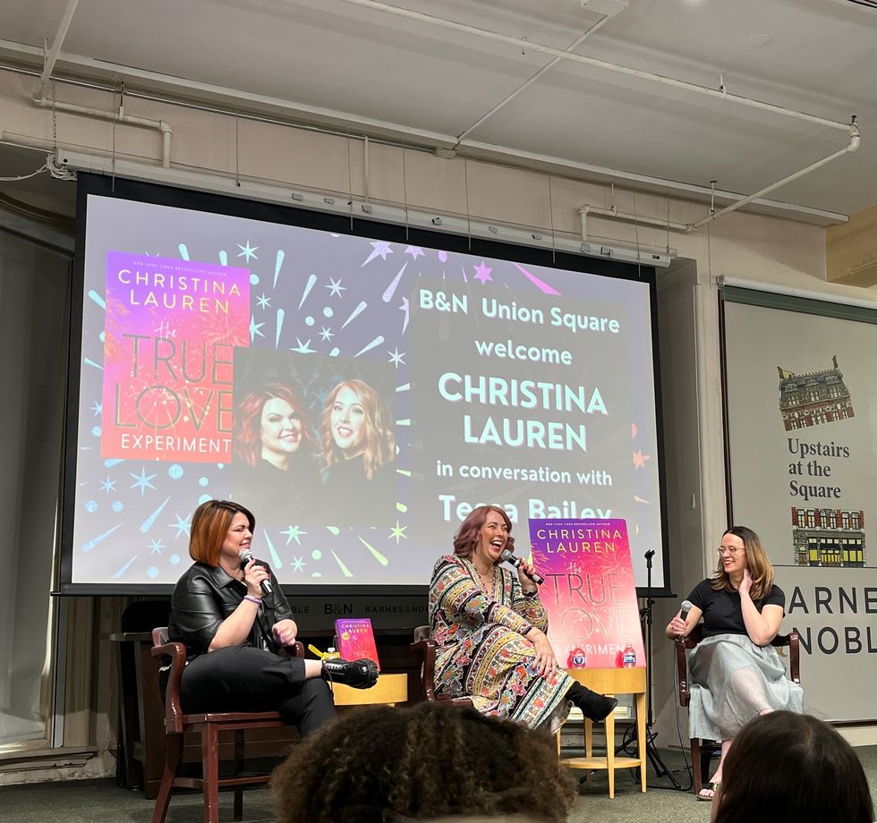 a group of women sitting on stools in front of a large screen