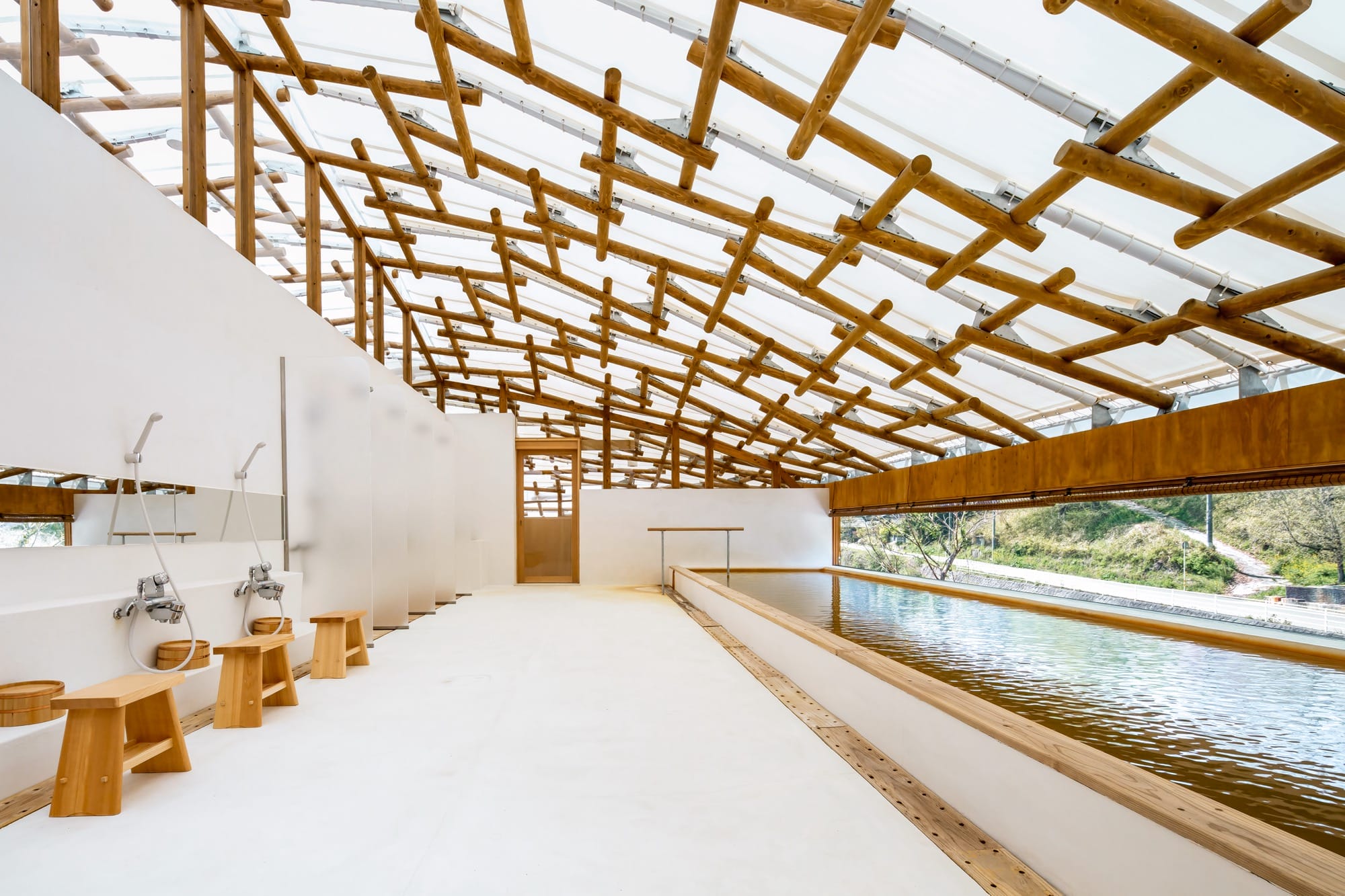 the interior of a large bathroom with a pool and a series of showers, bright white on the floor and walls with wooden latticework on the ceiling