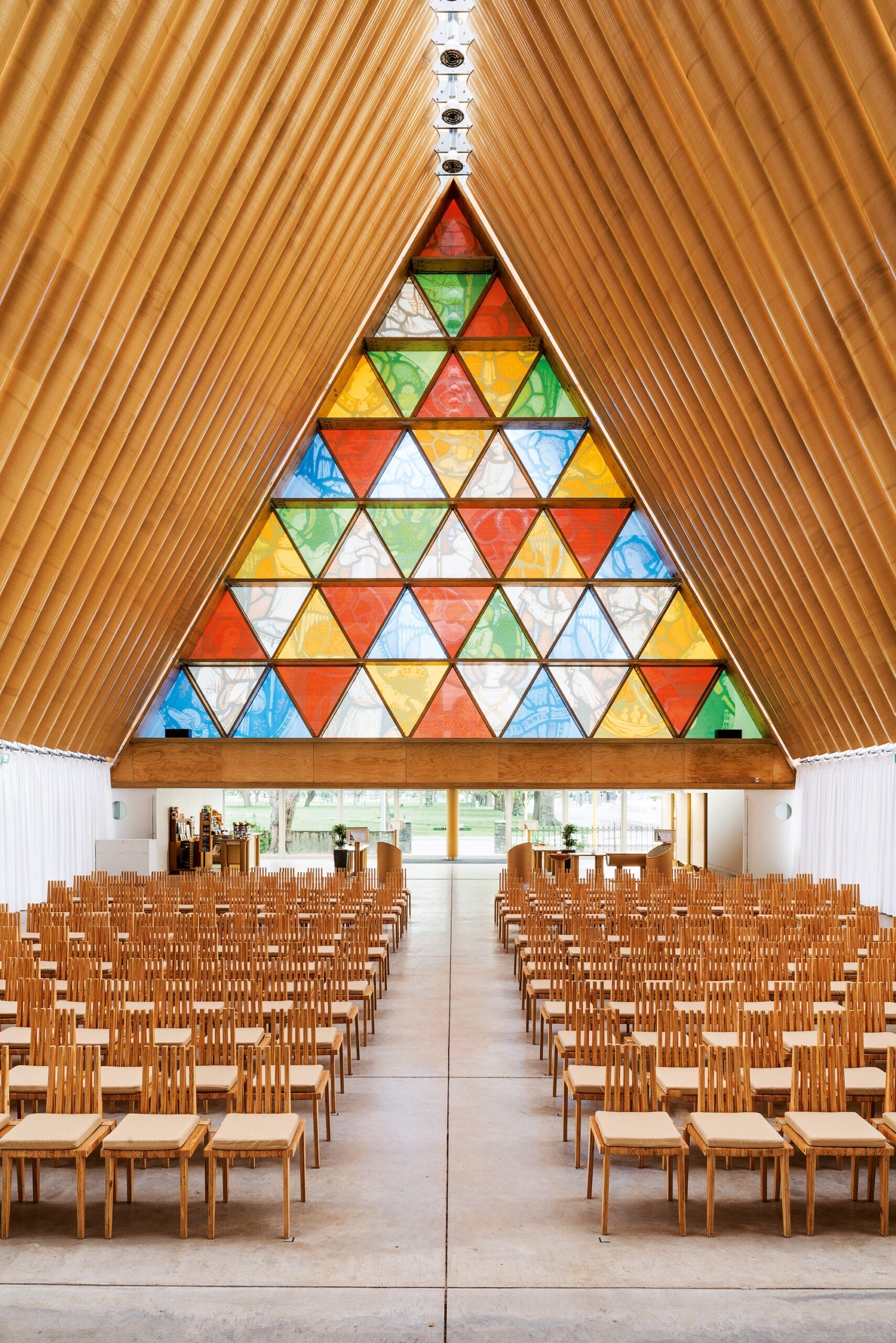 a church in New Zealand with a vaulted ceiling made of cardboard tubes and a large, triangular stained glass window made of numerous other small triangles of color