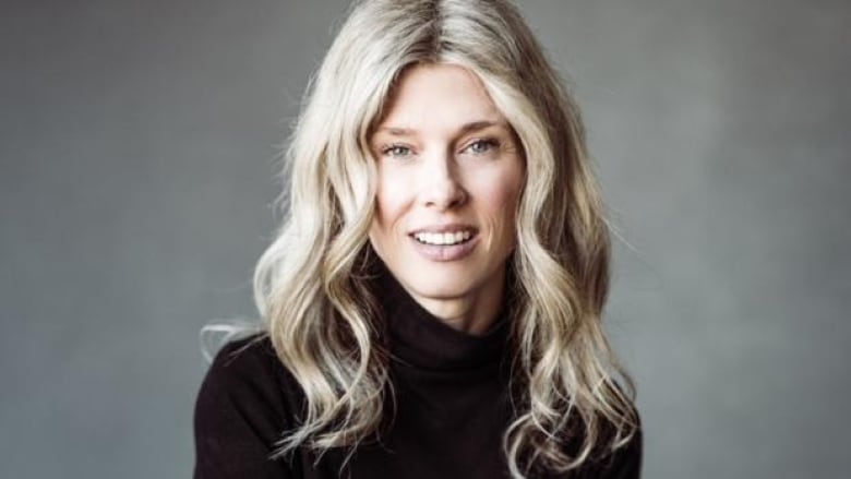 A woman with long blonde hair and a black turtleneck sweater smiling at the camera