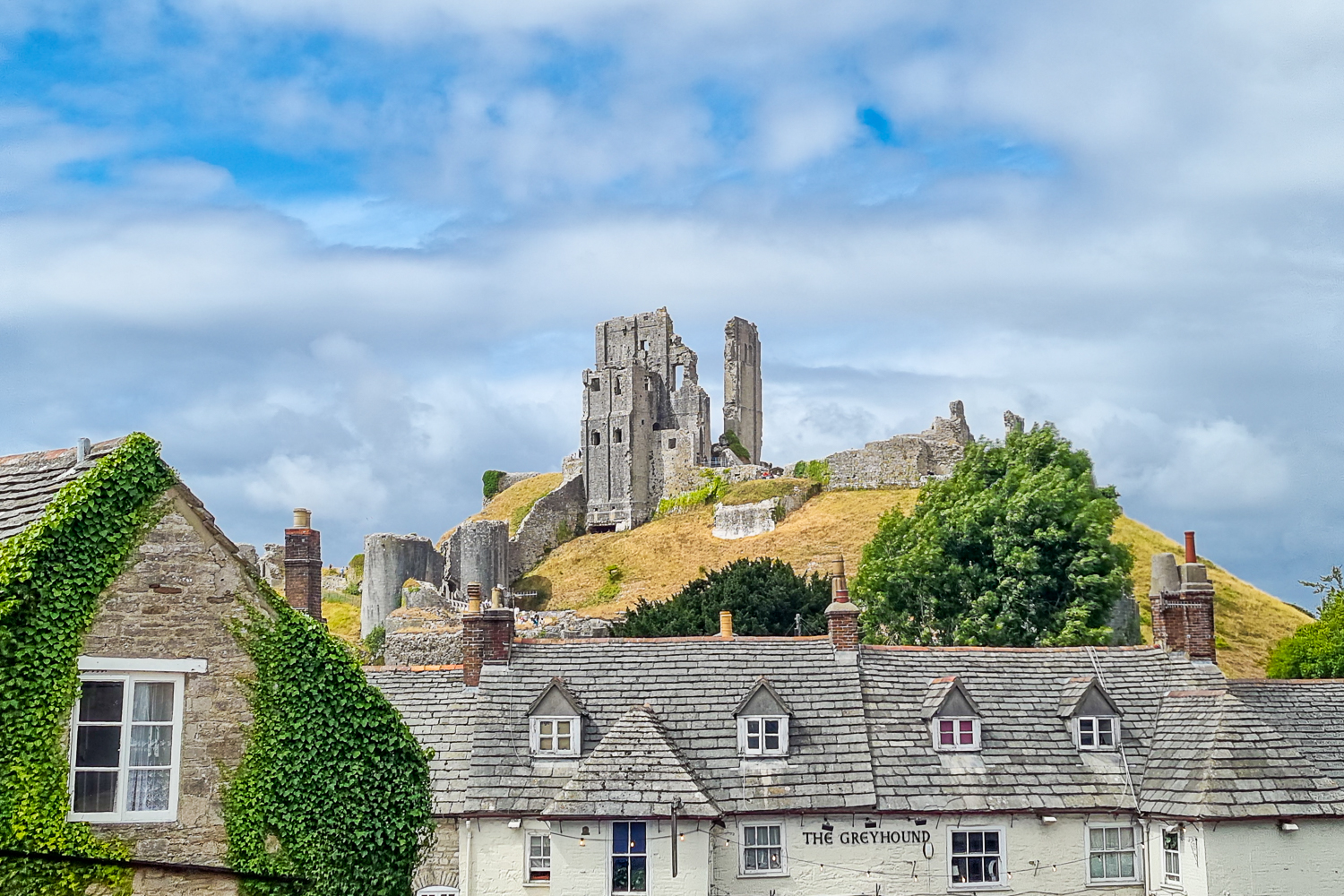 View from Corfe up to the ruins of the castle on its hill over The Greyhound pub - inspiration for Enid Blyton's Famous Five books, you'll find plenty of things to do during a day out in Dorset at Corfe Castle with kids