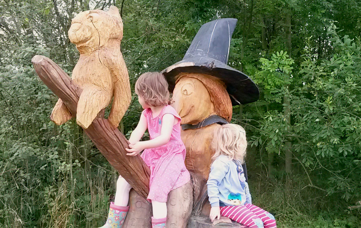 My daughter and her friend sit on the wooden witch sculpture with broom and dog - my review of the Room on the Broom trail in Yorkshire